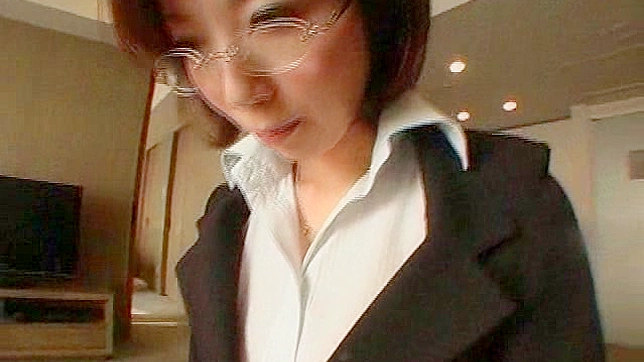 メガネをかけたショートヘアの日本人OLが室内でポーズをとっている。